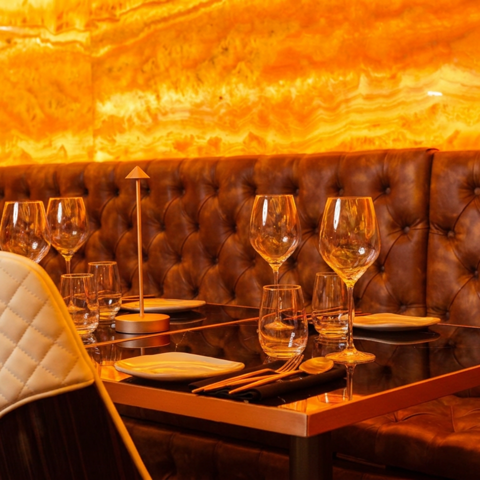 Elegant restaurant booth with tufted leather seating, set table, wine glasses, and warm amber lighting.