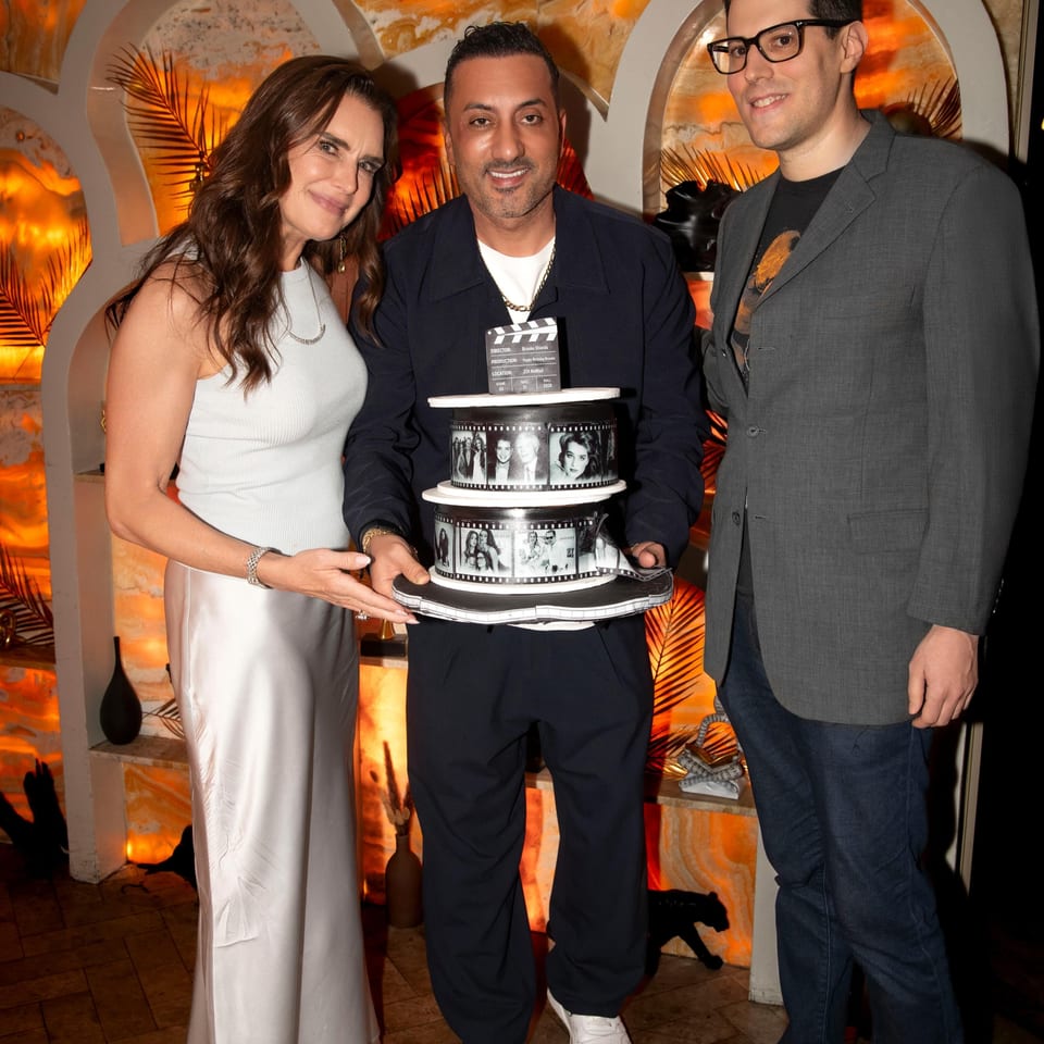 Three people pose at ZOI Mediterranean restaurant beside a film-themed celebration cake in a warmly lit interior.