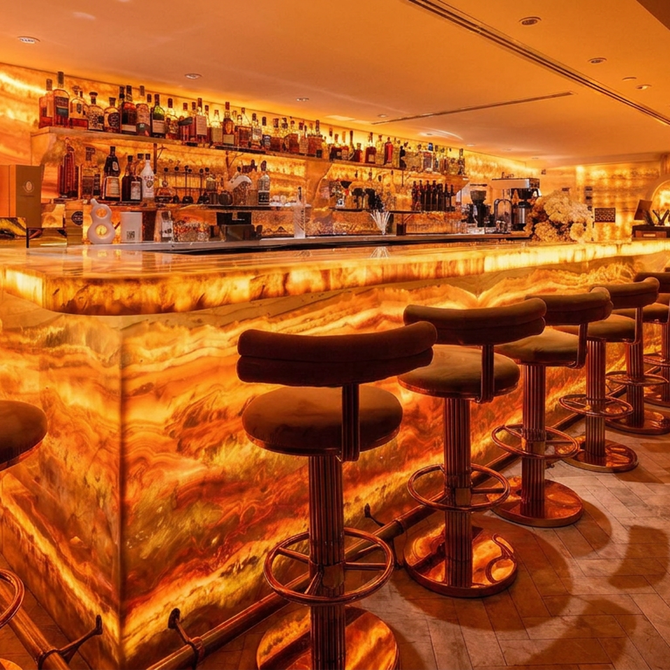 Luxurious amber-lit bar with glowing stone counters, rows of bottles, arched display shelves, and upholstered stools.