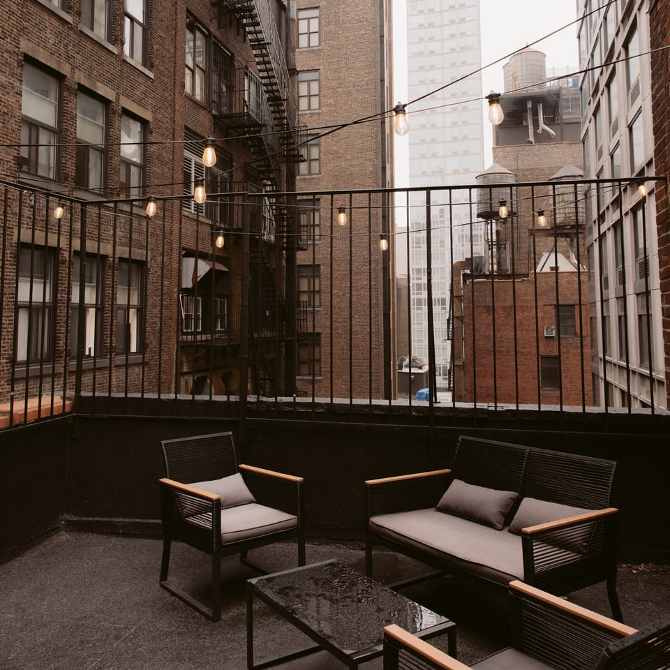 Rooftop patio with black lounge chairs, coffee table, string lights, and brick city buildings surrounding it.