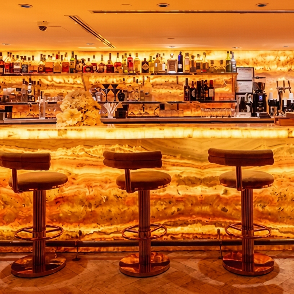 Warmly lit restaurant bar with glowing stone counter, five leather stools, liquor shelves, coffee equipment, and polished wood floors.