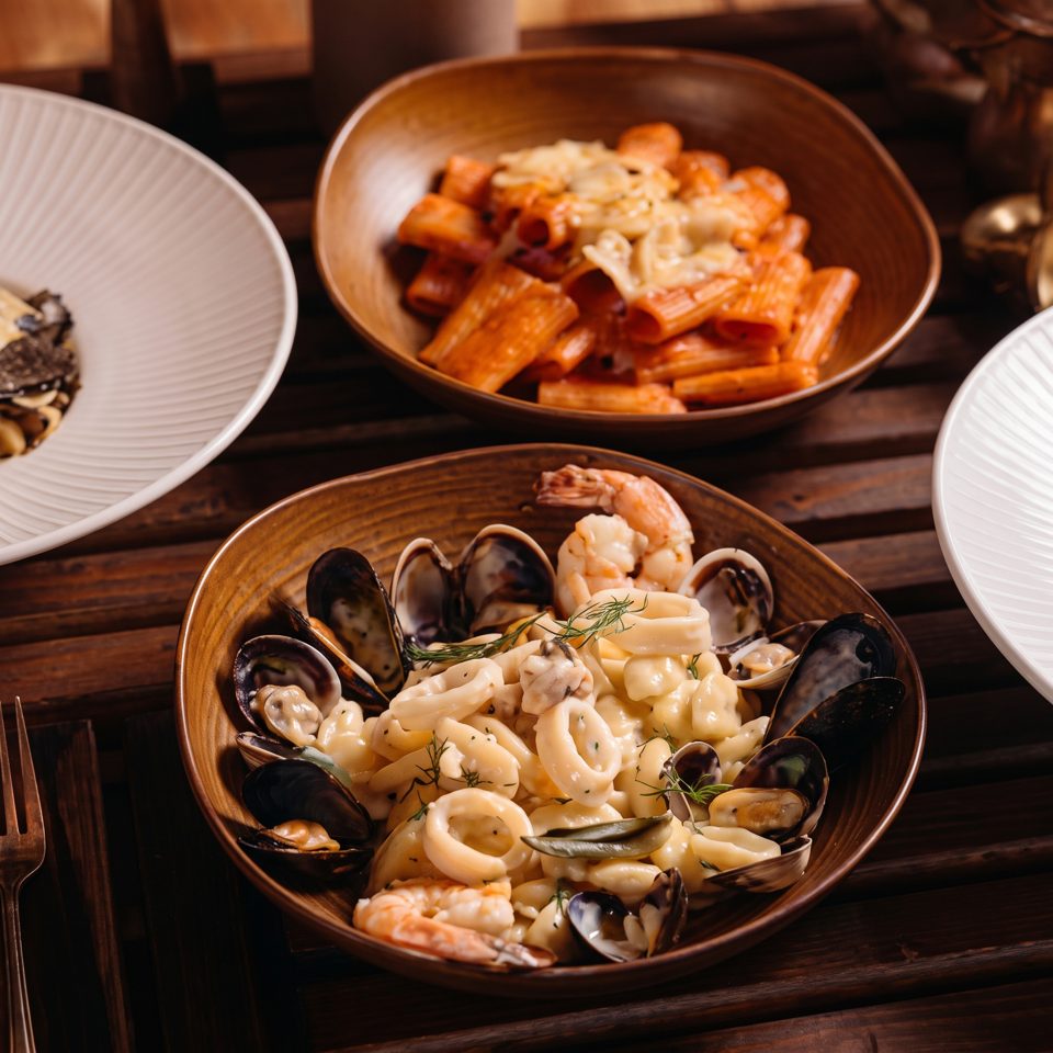 Creamy seafood pasta with mussels, shrimp, squid, and clams served in a bowl alongside tomato seafood pasta.